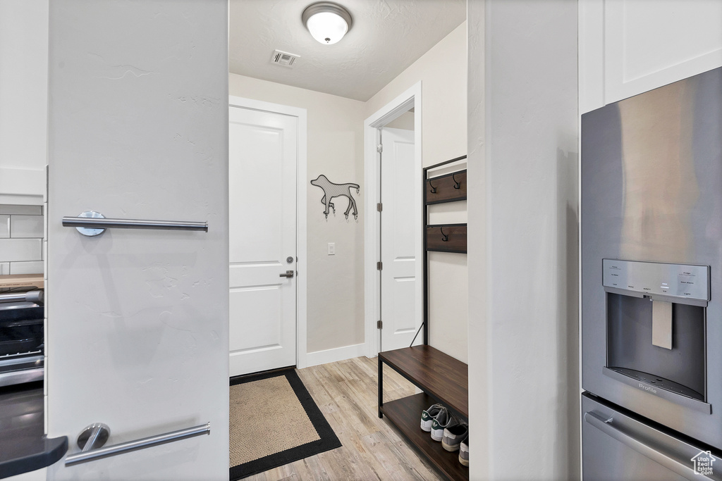 Interior space featuring light wood-style floors, visible vents, white cabinets, stainless steel fridge, and baseboards