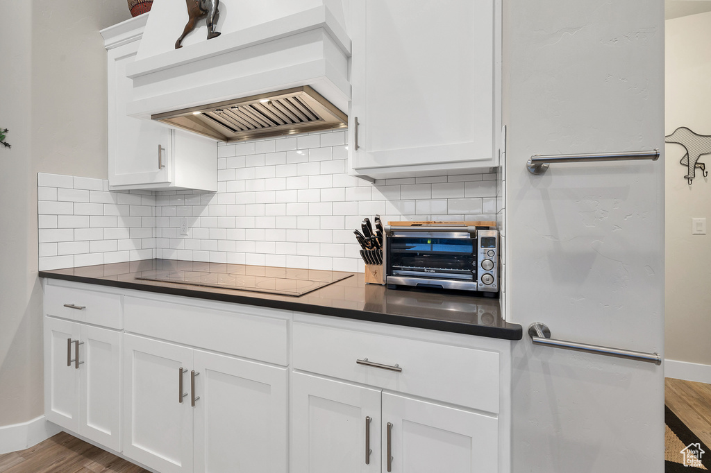Kitchen with custom exhaust hood, decorative backsplash, dark countertops, and black electric cooktop