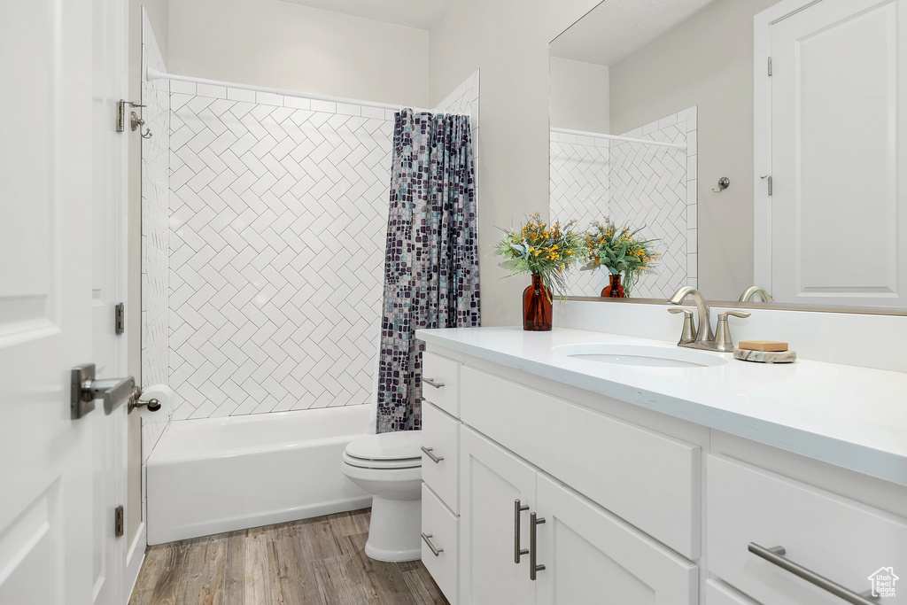 Full bath featuring shower / bath combination with curtain, vanity, toilet, and wood finished floors
