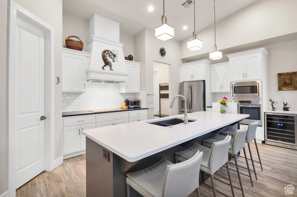 Kitchen featuring light wood-type flooring, a kitchen bar, stainless steel appliances, beverage cooler, and a sink