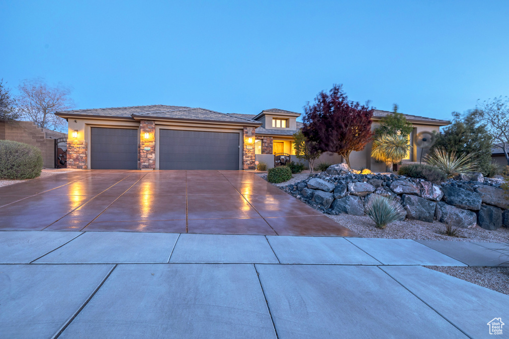 Prairie-style home featuring concrete driveway, stucco siding, stone siding, and a garage