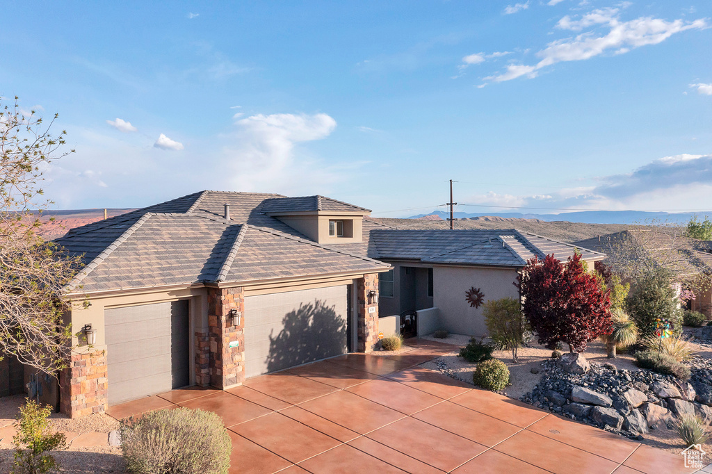 View of front of home with an attached garage, driveway, stucco siding, and stone siding