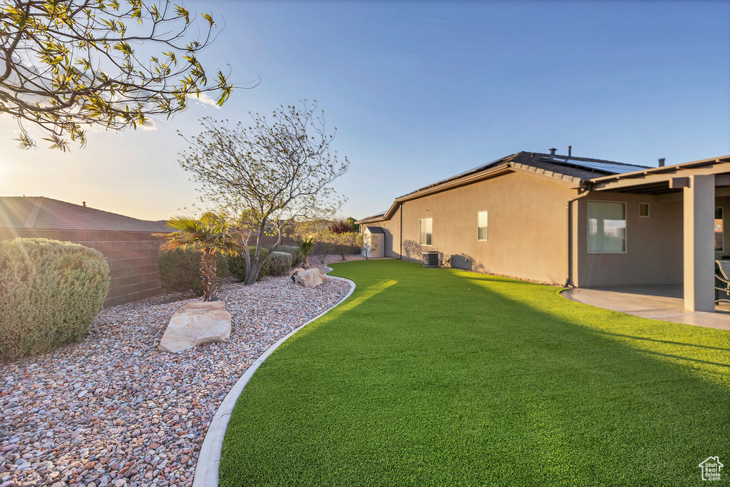 Yard at dusk with a patio area, a fenced backyard, and cooling unit