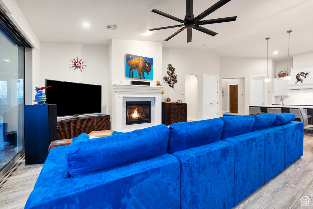 Living area featuring visible vents, ceiling fan, light wood finished floors, and a glass covered fireplace