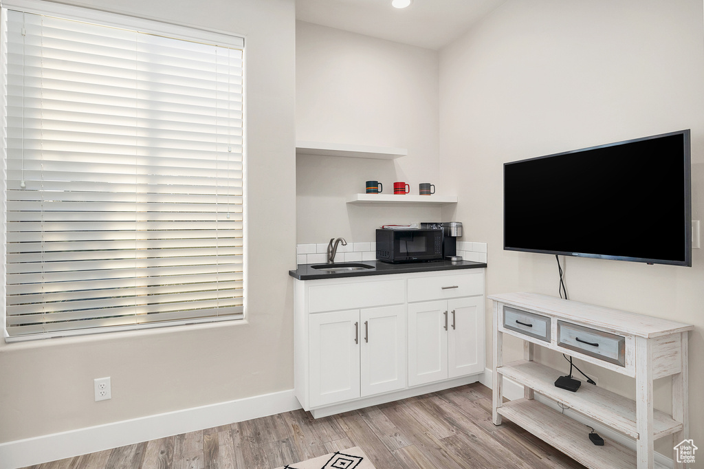 Interior space with black microwave, white cabinetry, open shelves, a sink, and light wood finished floors