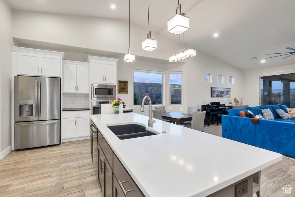 Kitchen featuring light wood-type flooring, appliances with stainless steel finishes, a sink, lofted ceiling, and open floor plan