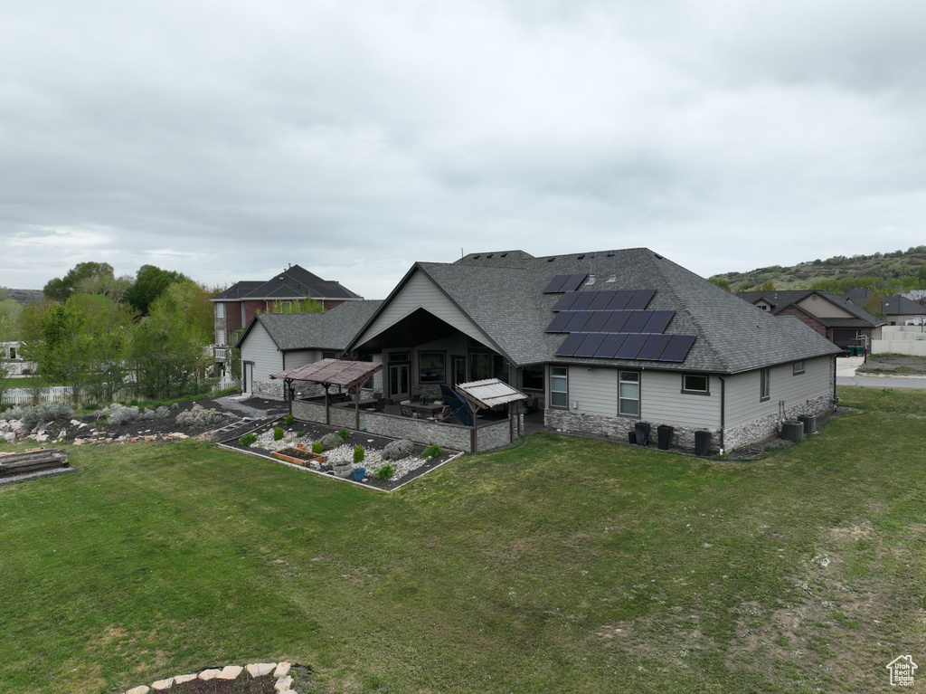 Back of house featuring a shingled roof, solar panels, a lawn, and a garden