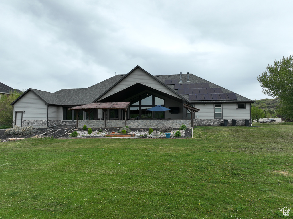 Back of property with a lawn, a shingled roof, and stone siding