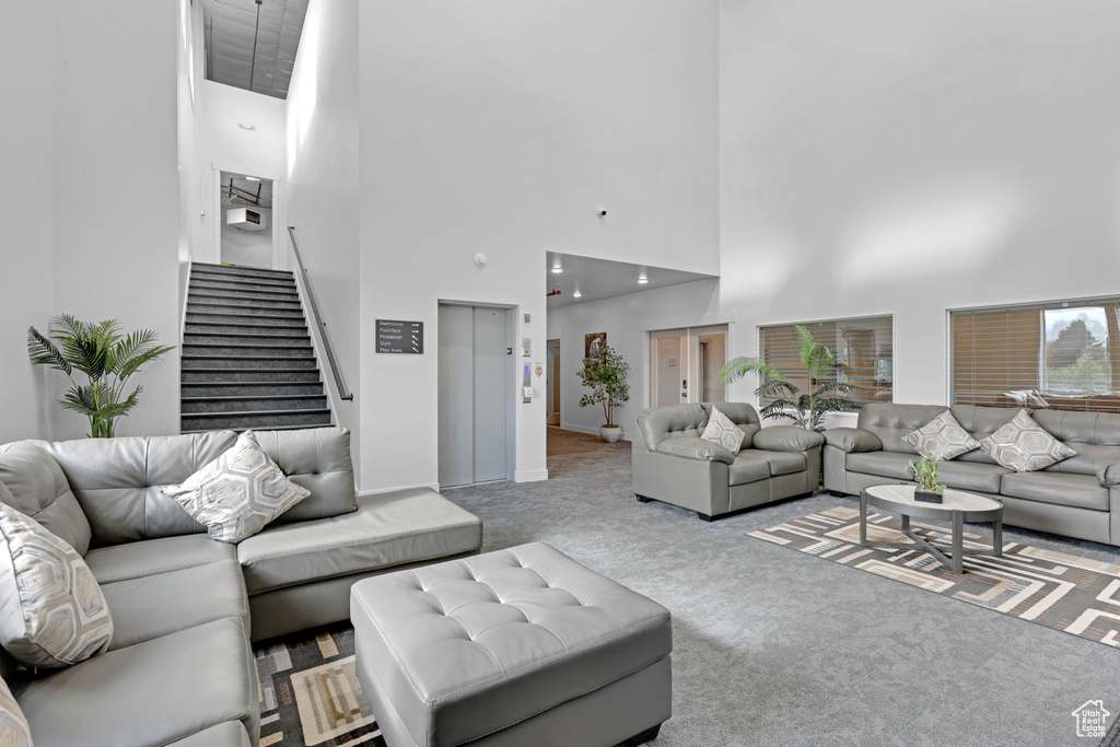 Carpeted living room featuring a high ceiling, stairway, elevator, and baseboards