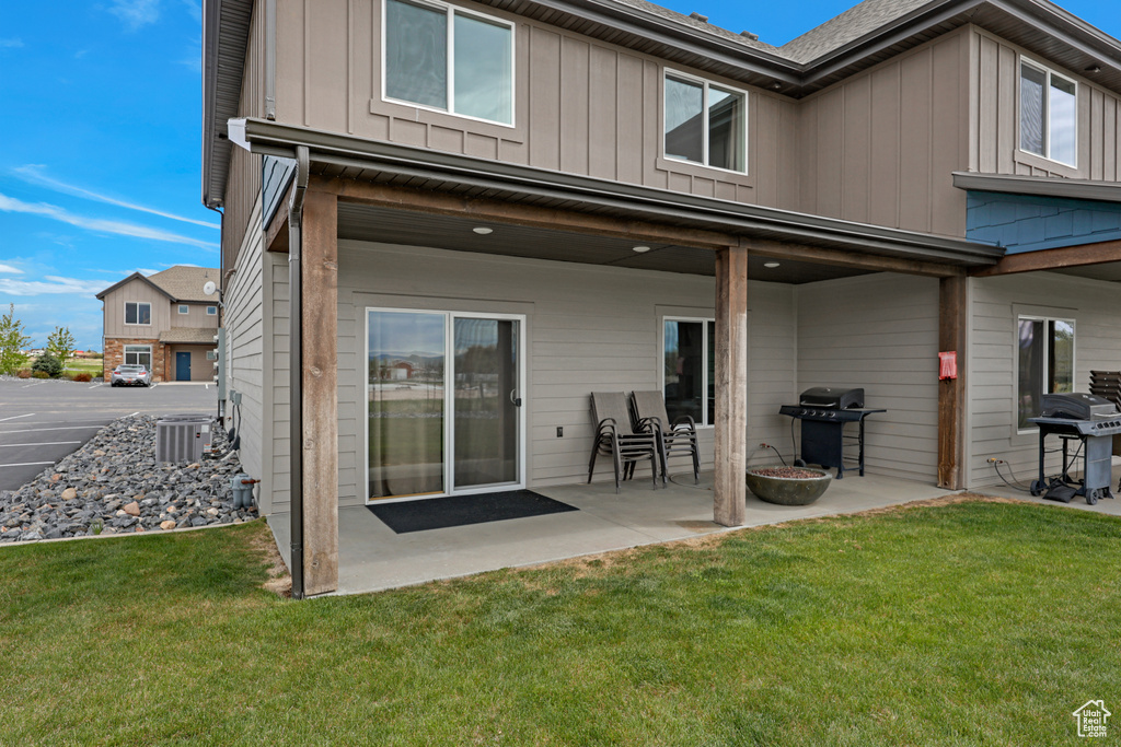 Back of house with board and batten siding, a patio, a yard, and central air condition unit