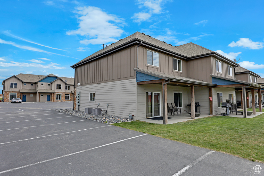 Back of property with board and batten siding, uncovered parking, a yard, cooling unit, and roof with shingles