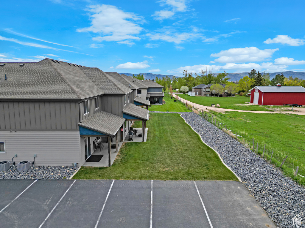 View of grassy yard featuring a mountain view, a patio area, central AC unit, and a residential view