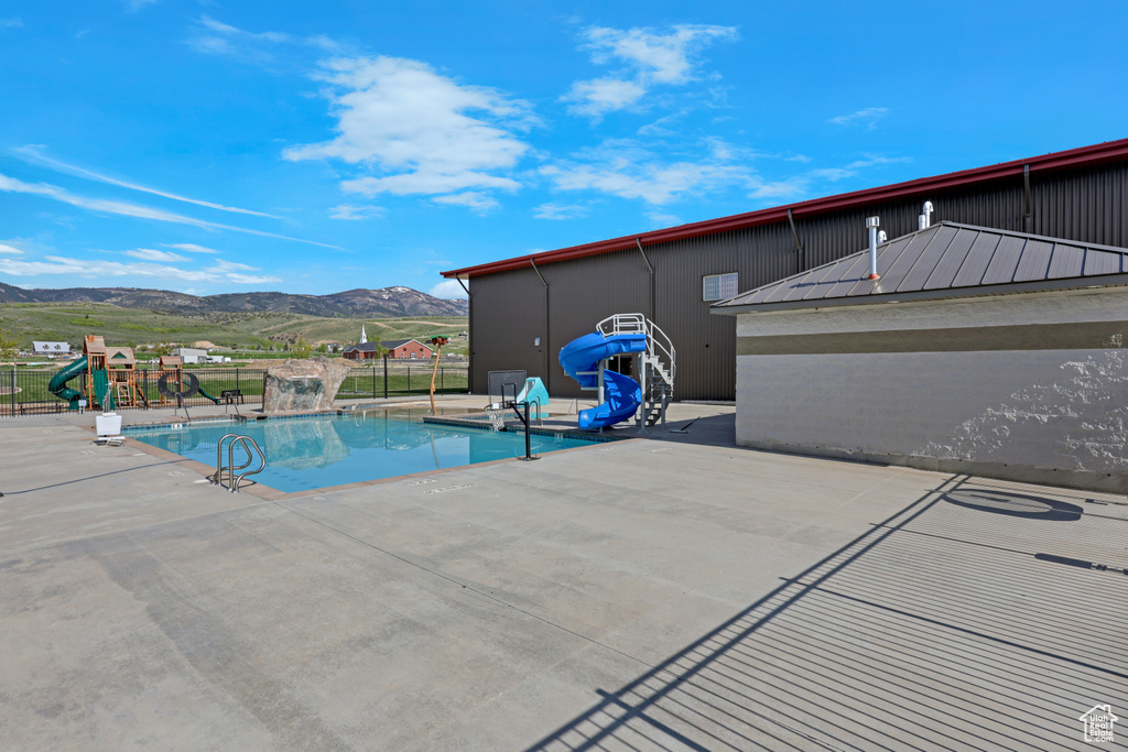 Community pool featuring a water slide, a mountain view, and a patio area