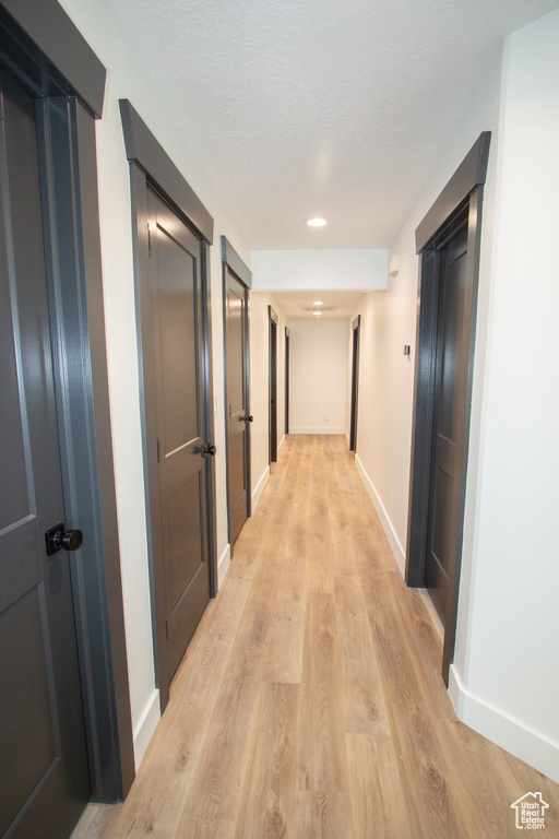 Hallway with light wood-type flooring, recessed lighting, baseboards, and a textured ceiling