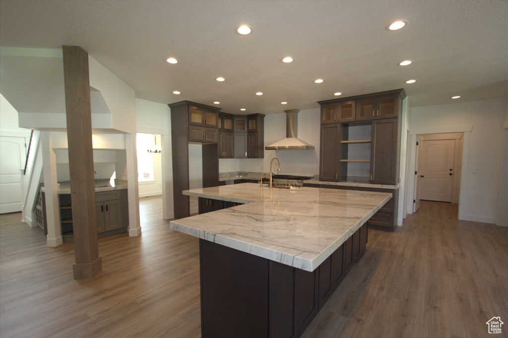 Kitchen featuring wall chimney range hood, recessed lighting, wood finished floors, and a spacious island