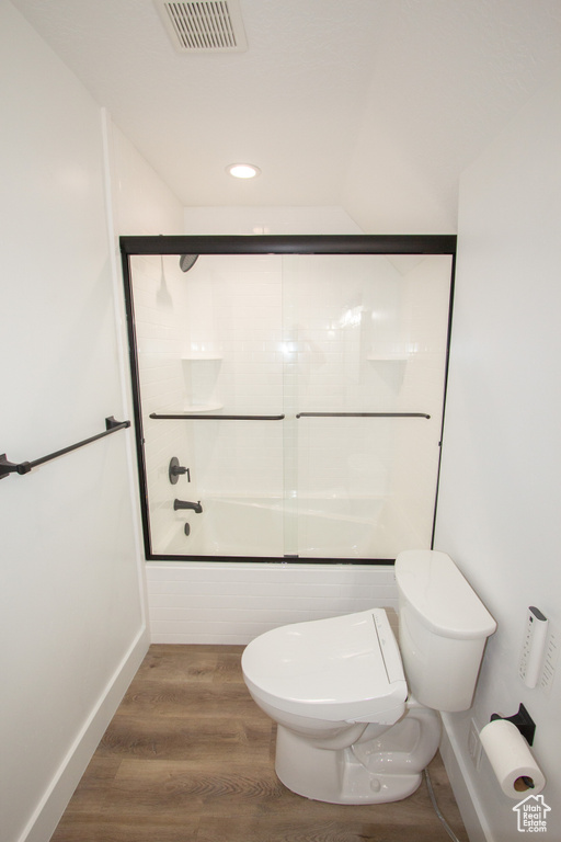 Full bath with shower / bath combination with glass door, visible vents, toilet, wood finished floors, and baseboards