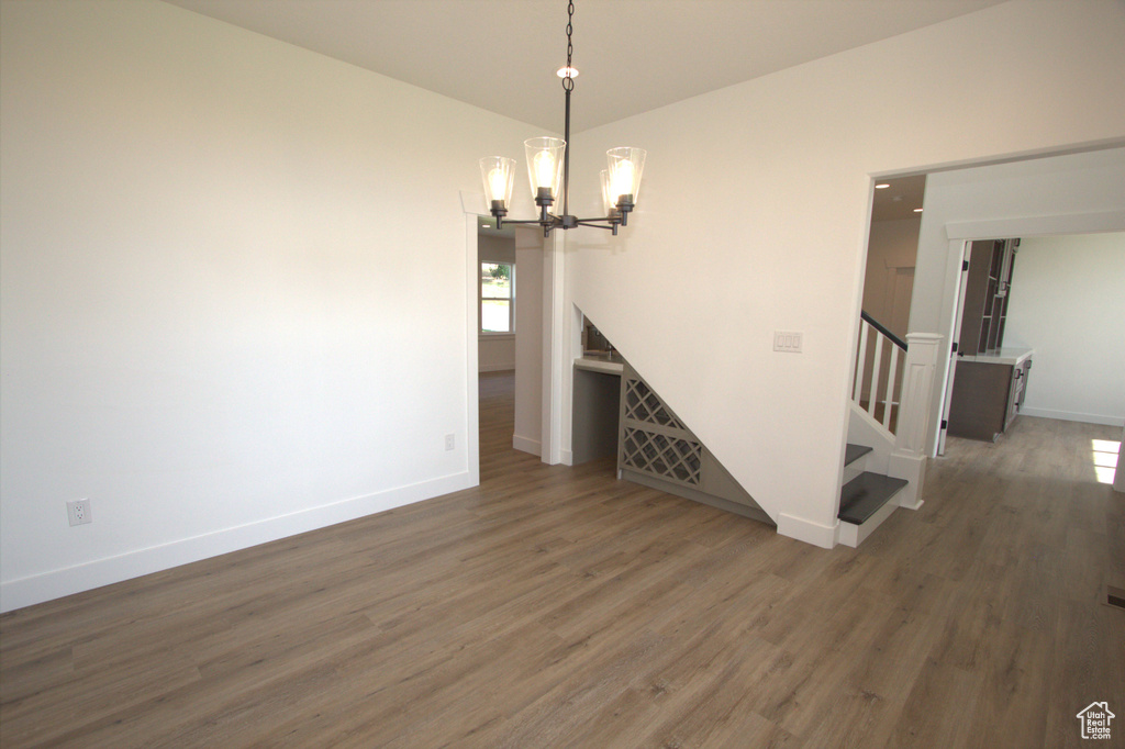 Unfurnished dining area featuring wood finished floors, a notable chandelier, baseboards, and stairway