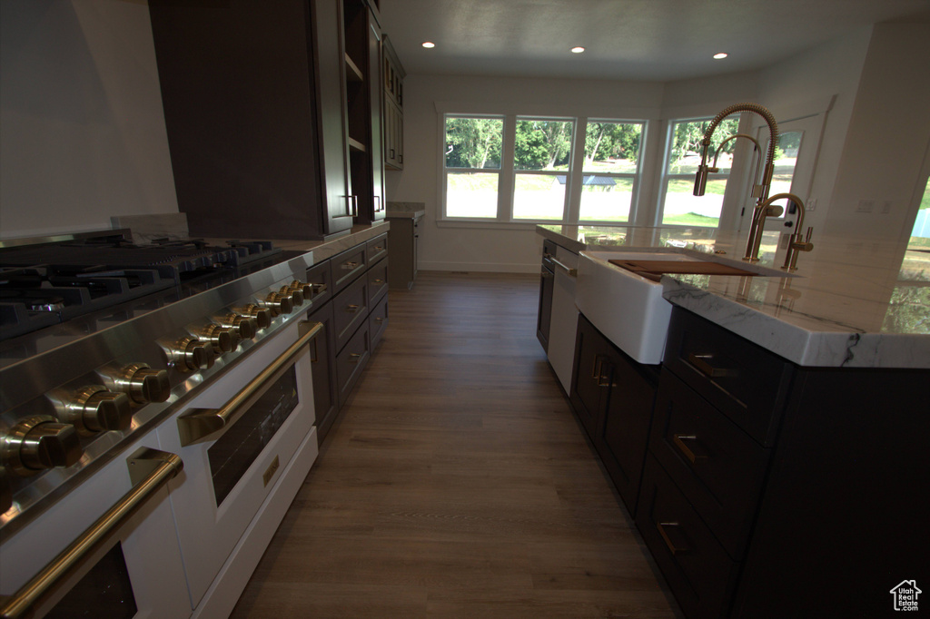 Kitchen featuring a sink, an island with sink, wood finished floors, light stone countertops, and high end range