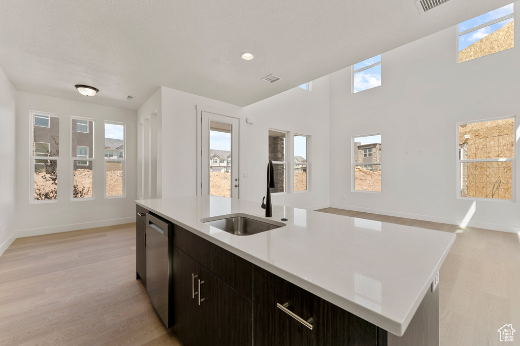 Kitchen with light wood finished floors, light countertops, a center island with sink, stainless steel dishwasher, and open floor plan