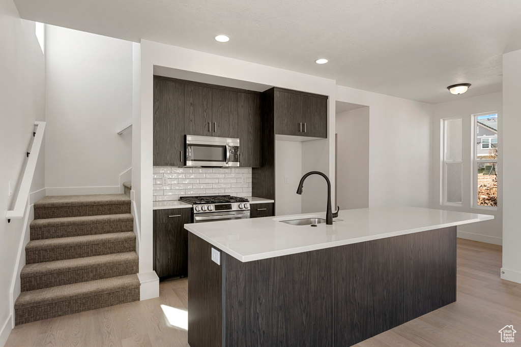 Kitchen with appliances with stainless steel finishes, light countertops, decorative backsplash, light wood finished floors, and a center island with sink