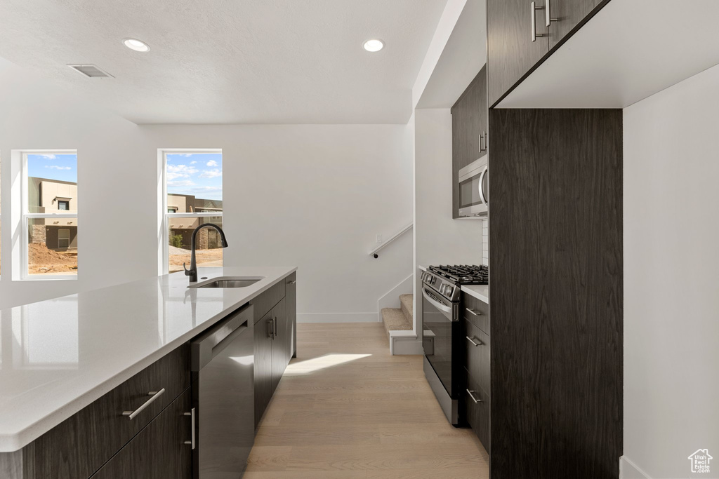 Kitchen with appliances with stainless steel finishes, light wood finished floors, light countertops, modern cabinets, and recessed lighting