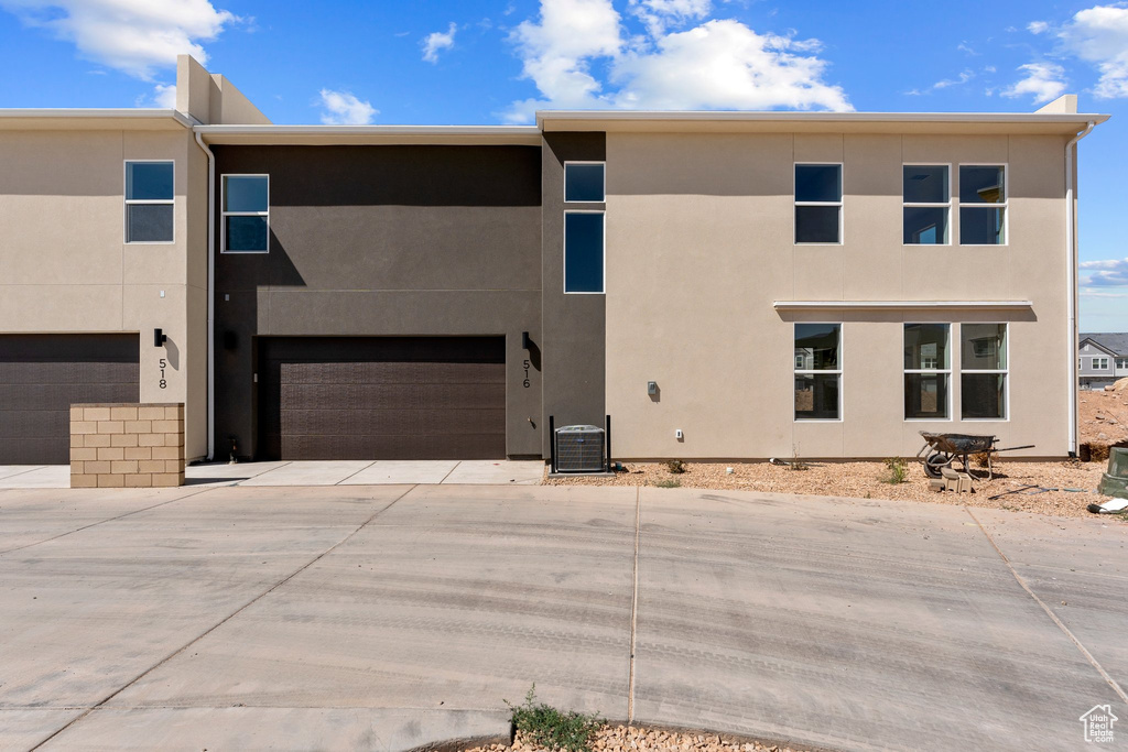 Rear view of property with driveway, an attached garage, and stucco siding