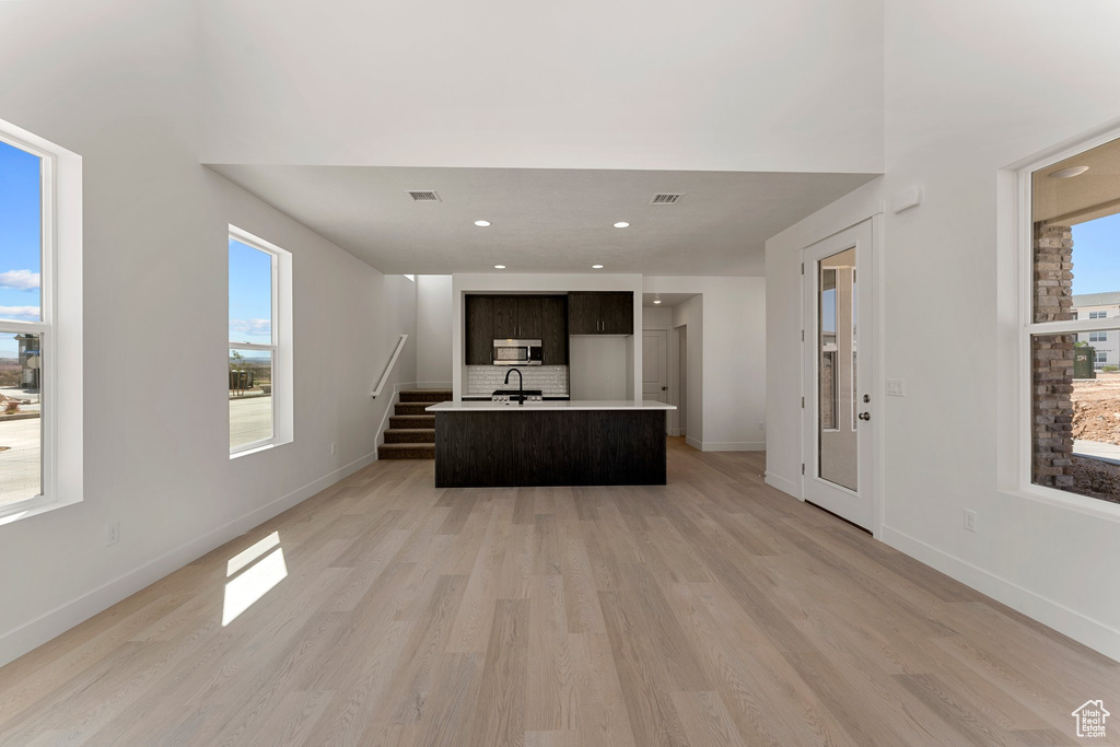 Kitchen with light countertops, light wood-style floors, stainless steel microwave, a center island with sink, and backsplash