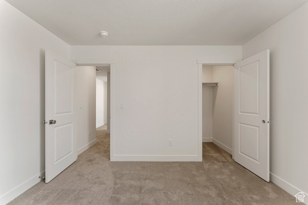 Unfurnished bedroom with light carpet, a walk in closet, and a closet