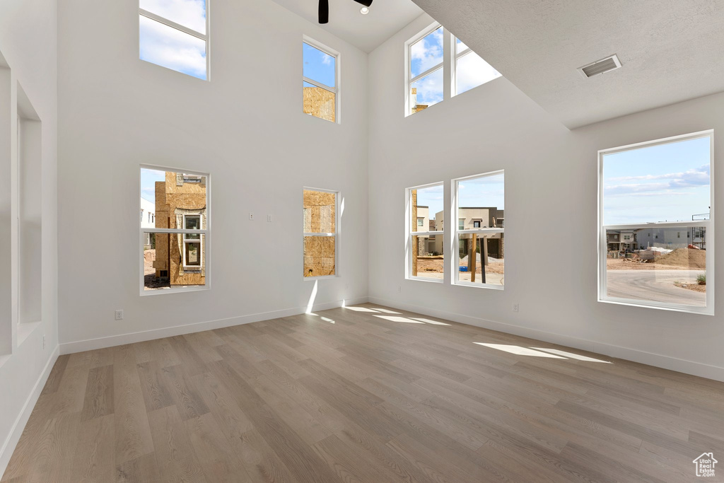 Unfurnished living room featuring light wood finished floors, ceiling fan, and a high ceiling