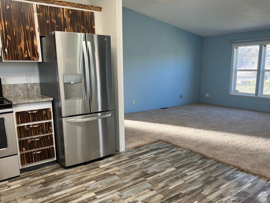 Kitchen with dark colored carpet, dark brown cabinetry, light countertops, dark wood-type flooring, and appliances with stainless steel finishes