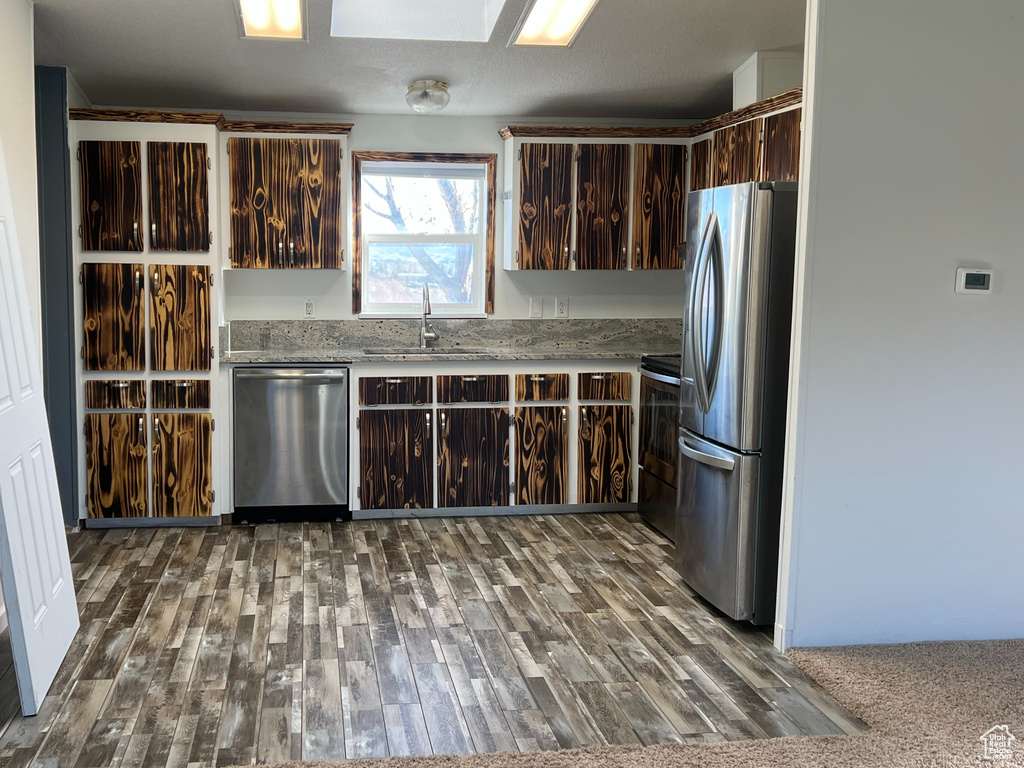 Kitchen with dark brown cabinetry, dark wood-style flooring, a sink, and appliances with stainless steel finishes