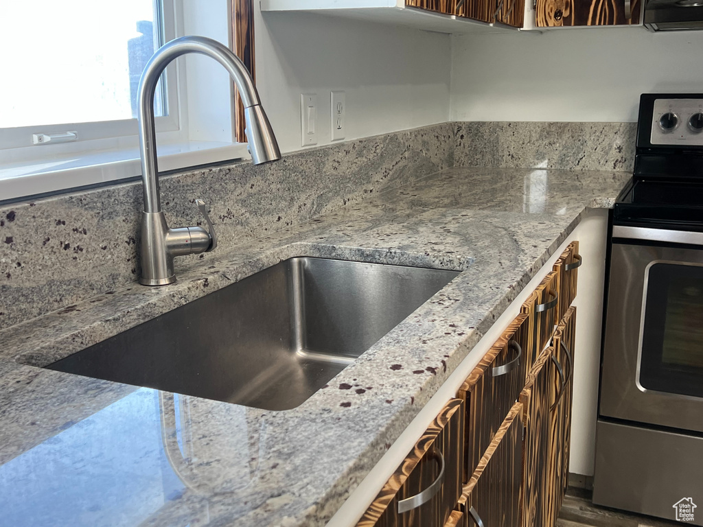 Kitchen with stainless steel electric range oven, light stone counters, and a sink
