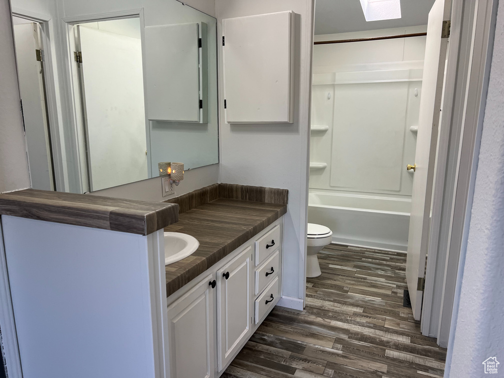 Bathroom featuring toilet, vanity, wood finished floors, and a skylight