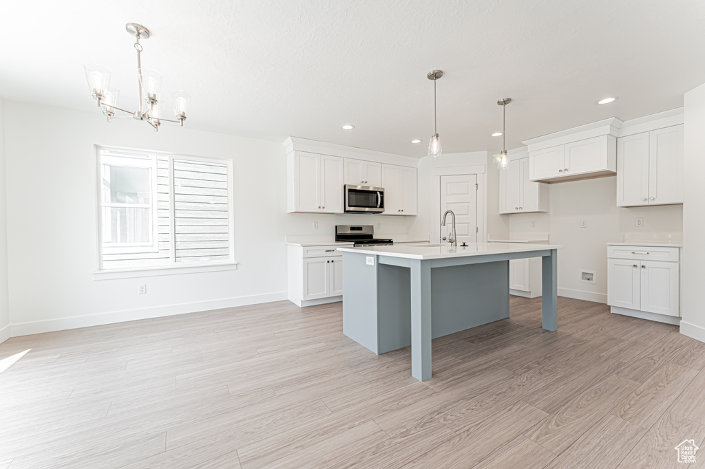 Kitchen with appliances with stainless steel finishes, a chandelier, light wood-style floors, light countertops, and white cabinets
