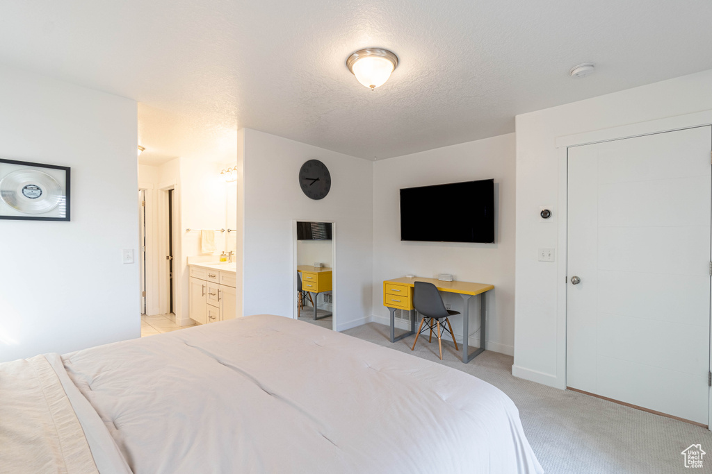 Bedroom featuring a textured ceiling, light colored carpet, baseboards, and ensuite bath
