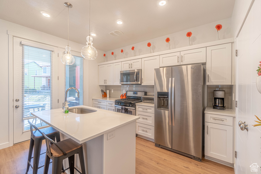 Kitchen featuring a sink, light wood-type flooring, a center island with sink, and stainless steel appliances