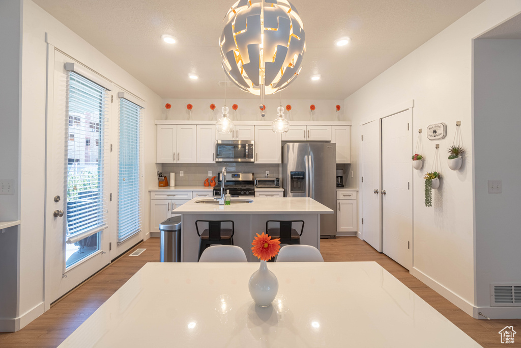 Kitchen featuring a sink, light wood-type flooring, appliances with stainless steel finishes, a kitchen island with sink, and decorative backsplash