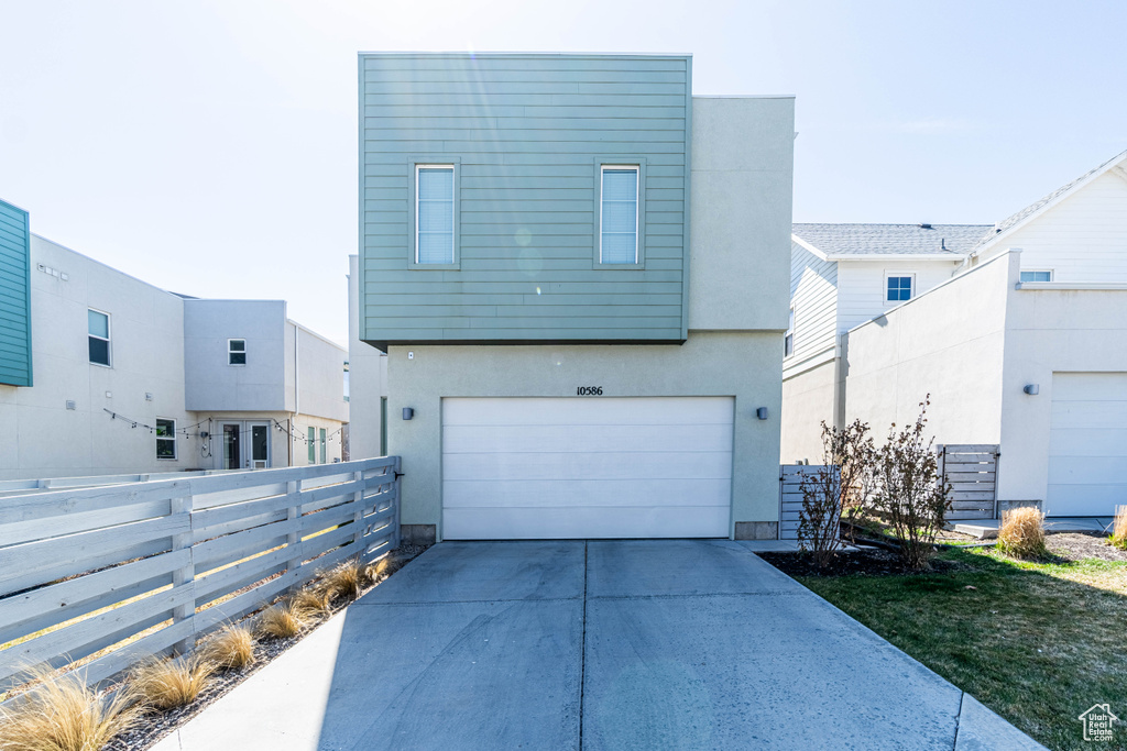 View of front of property featuring an attached garage, fence, driveway, and stucco siding
