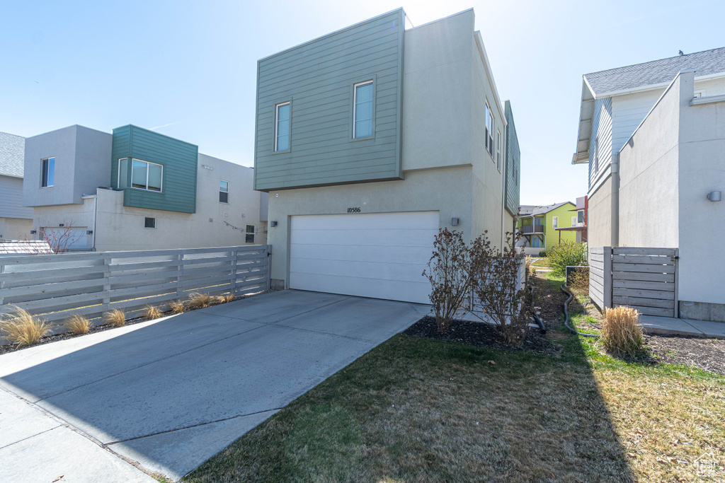 View of front of home featuring driveway, stucco siding, fence, and an attached garage