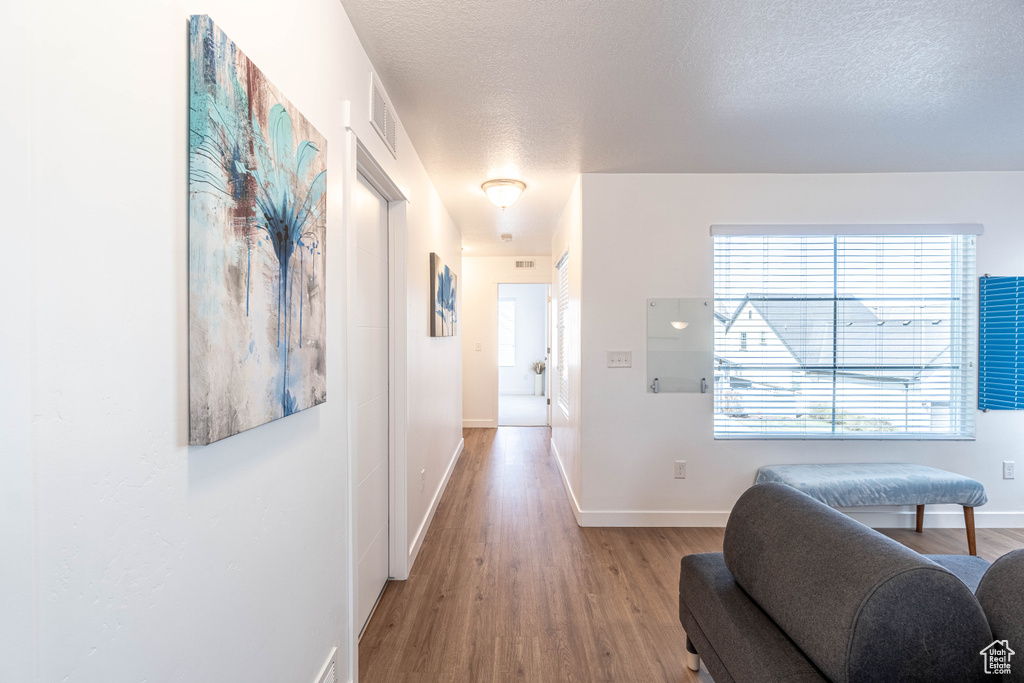 Hall featuring a textured ceiling, wood finished floors, baseboards, and visible vents
