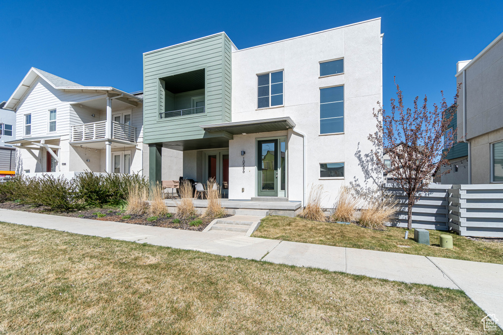 View of front of house featuring a front lawn, a balcony, and stucco siding