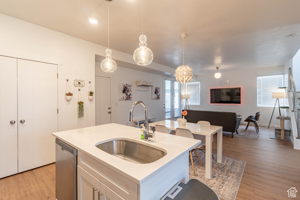Kitchen with light wood-type flooring, dishwasher, a sink, light countertops, and open floor plan