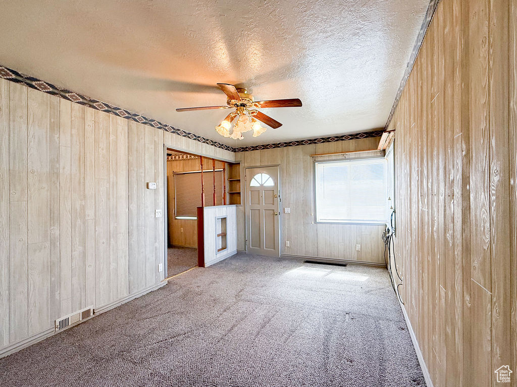 Empty room featuring ceiling fan, a textured ceiling, visible vents, carpet floors, and wooden walls