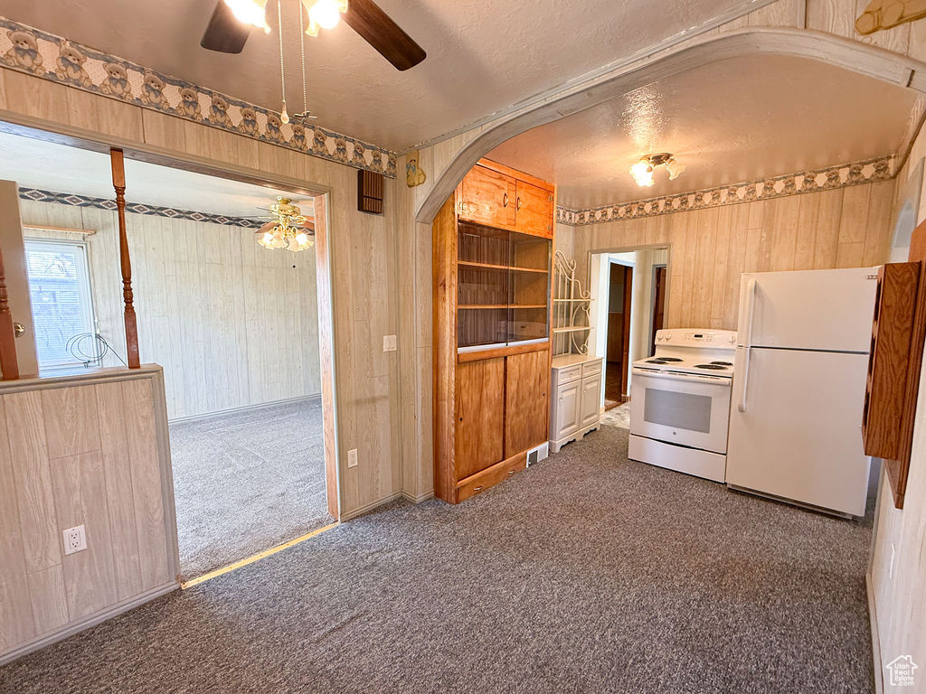Kitchen with white appliances, arched walkways, a textured ceiling, a ceiling fan, and carpet floors