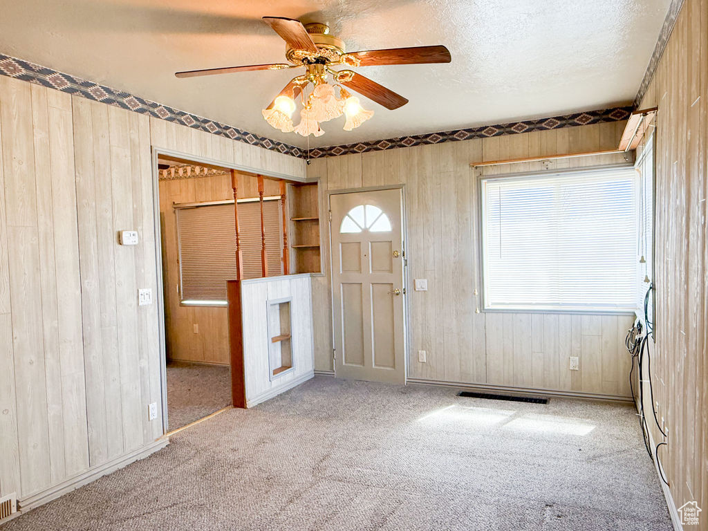 Carpeted empty room with wooden walls, a textured ceiling, and a ceiling fan