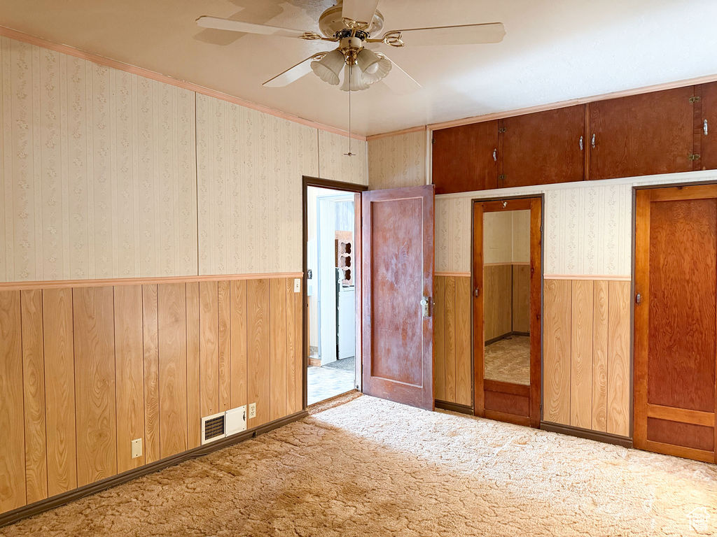Unfurnished bedroom with carpet, a ceiling fan, visible vents, a wainscoted wall, and wallpapered walls