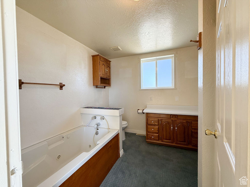 Bathroom featuring a textured ceiling, vanity, visible vents, toilet, and a jetted tub