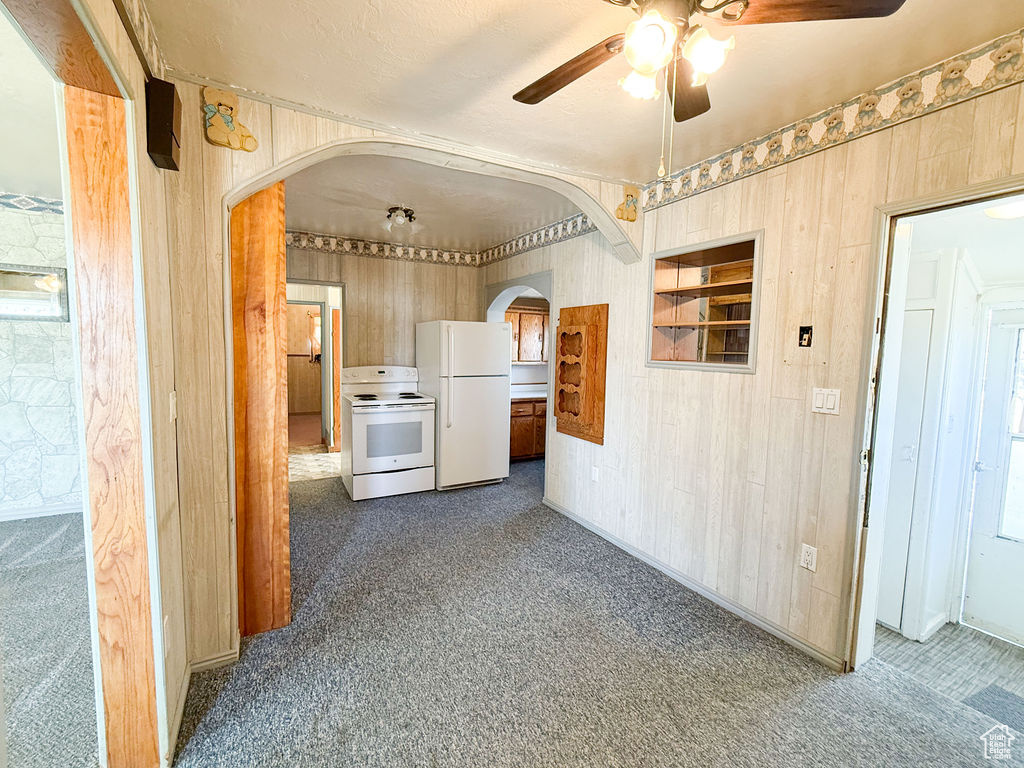 Kitchen with arched walkways, white appliances, wooden walls, and ceiling fan