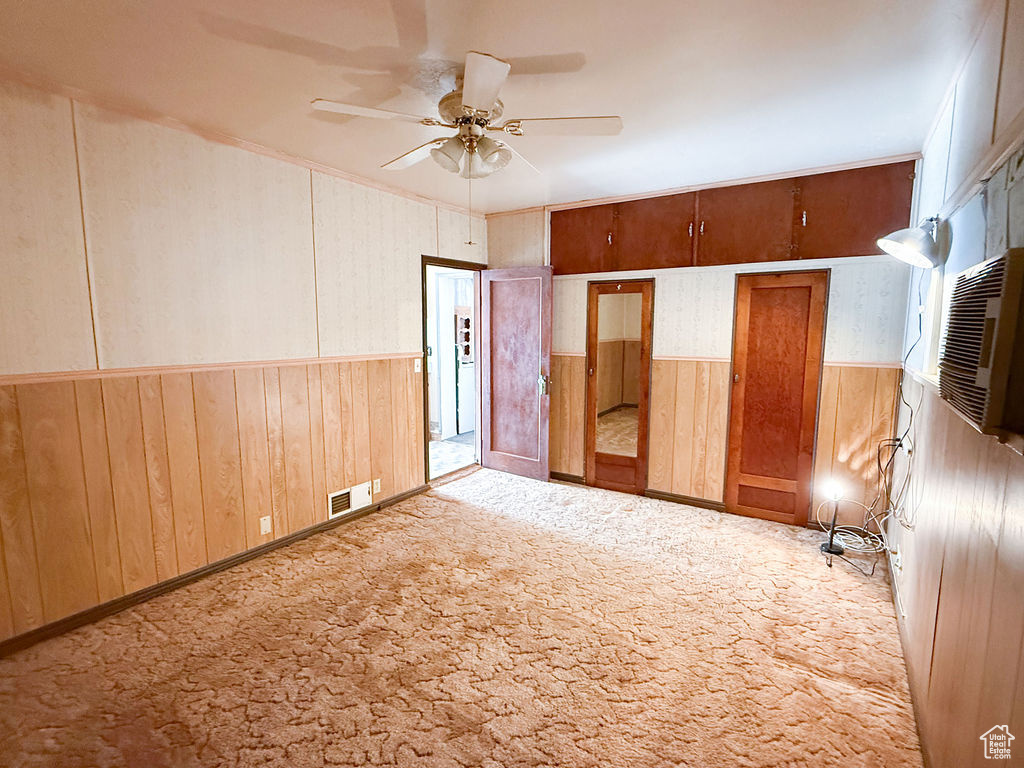 Carpeted empty room with wood walls, a ceiling fan, visible vents, and a wainscoted wall