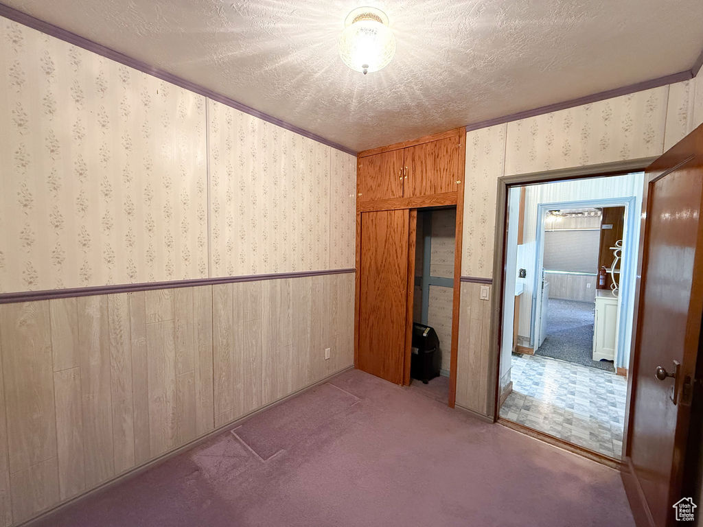 Unfurnished bedroom featuring a closet, a textured ceiling, wallpapered walls, a wainscoted wall, and carpet flooring